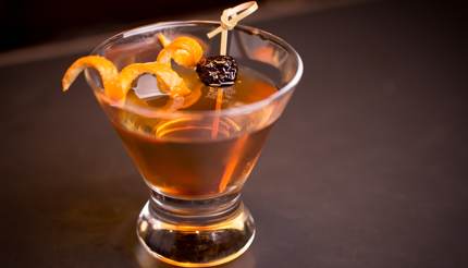 A cocktail with an orange peel and a cherry